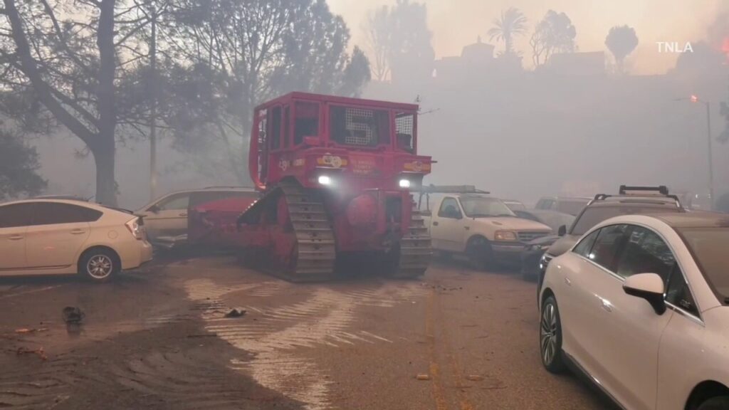 Bulldozers remove abandoned cars from road as fire burns in Southern California