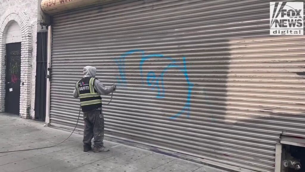 Man paints over graffiti on vandalized garage door in downtown Los Angeles